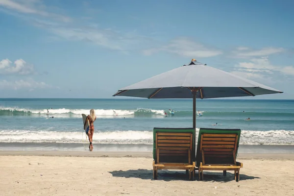 Sombrilla de playa con tumbonas contra el océano con surfistas — Foto de Stock