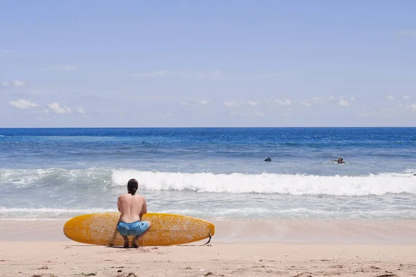 Surfista sentado en la playa de arena mirando al océano — Foto de Stock