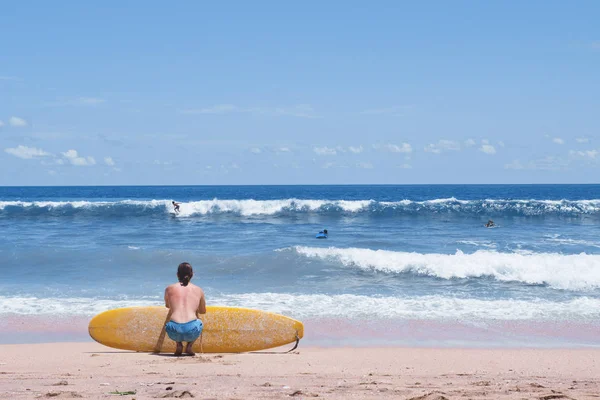 Surfista sentado en la playa de arena mirando al océano — Foto de Stock