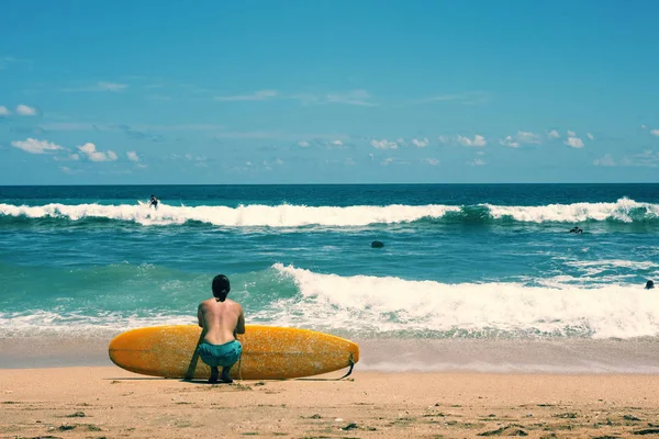 Surfista sentado en la playa de arena mirando al océano — Foto de Stock