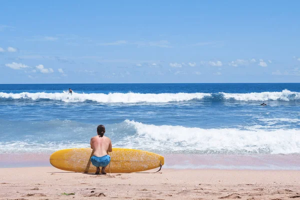 Surfista sentado en la playa de arena mirando al océano — Foto de Stock