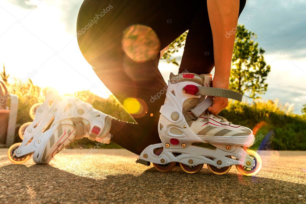 A woman tightens roller skates on the path. Womans legs with roller blades at sunny day.