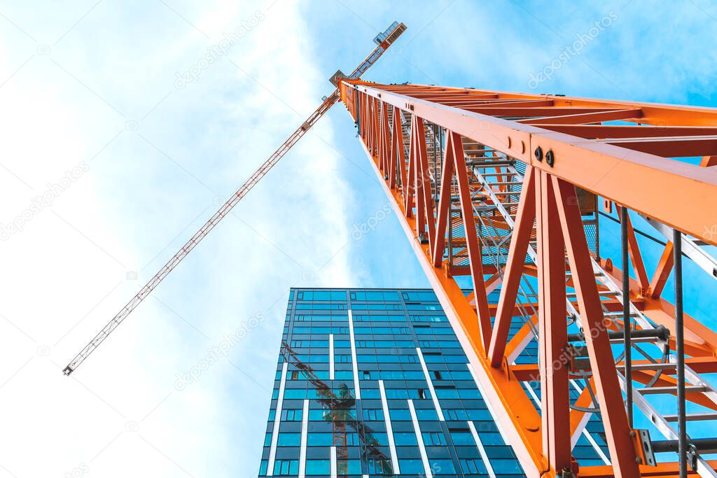 Yellow tower crane. Bottom view of a tall construction crane next to a modern building.
