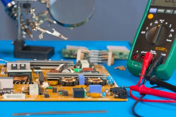 The workplace of the TV repair engineer before starting work. On the table is a power supply unit from the TV, a multimeter and electronic parts.