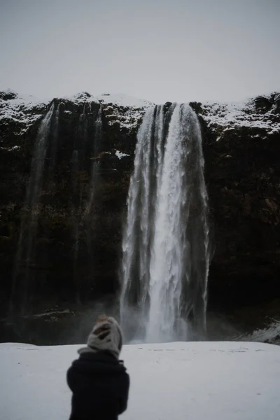 一个戴头巾的人正站在冰岛 Seljalandsfoss 的前面 在冬天的中间 图库图片