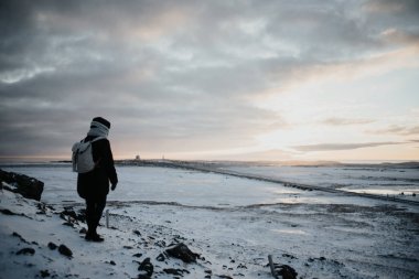 Bir tepenin üstünde duran bir kişi, kar üzerinde seyir Stokksnes, İzlanda manzara günbatımında kaplı.