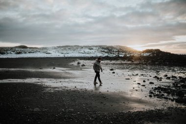 Stokksnes, İzlanda günbatımında bir siyah kum Plajı üzerinde yürüyen bir insan.