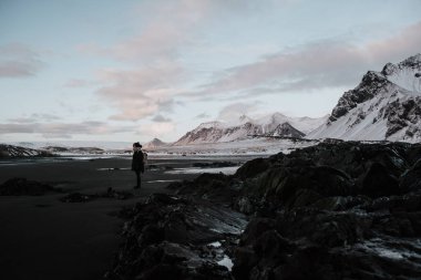 Stokksnes, İzlanda karlı manzara önünde siyah bir kum Plajı üzerinde duran bir kişi