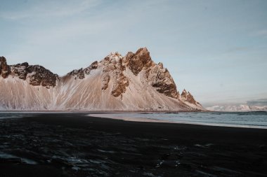 Bazı karla kaplı dağlar gün batımında önünde siyah kum plaj, Stokksnes, İzlanda.