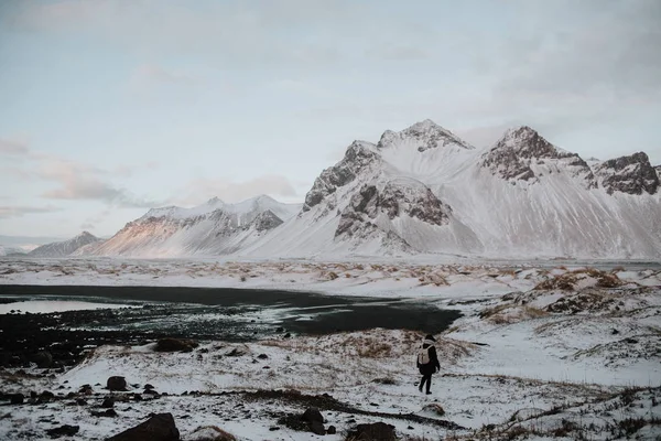 一个人走过积雪覆盖的领域对 Stokksnes 冰岛的黑色沙滩 — 图库照片