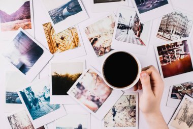 Bir avuç polaroid arasında kahve bardağı tutan bir el.