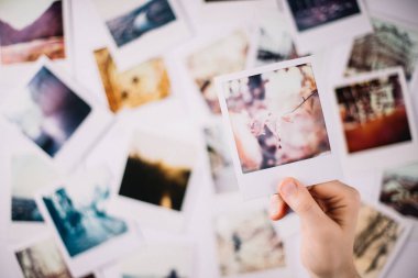 Bulanık arka planda bir grup polaroid üzerinde bir polaroid tutan bir el
