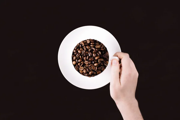 暗い背景にコーヒー豆で満たされたマグカップの手に達する — ストック写真