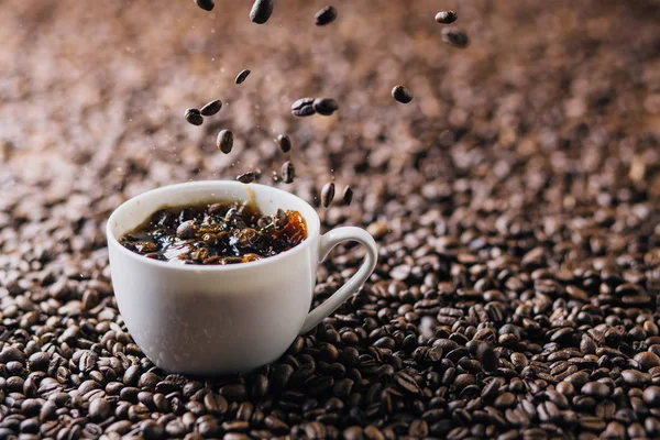 コーヒー豆が完全にコーヒー豆で構成されている背景にコーヒーで満たされたマグカップに飛び散るコーヒー豆 — ストック写真