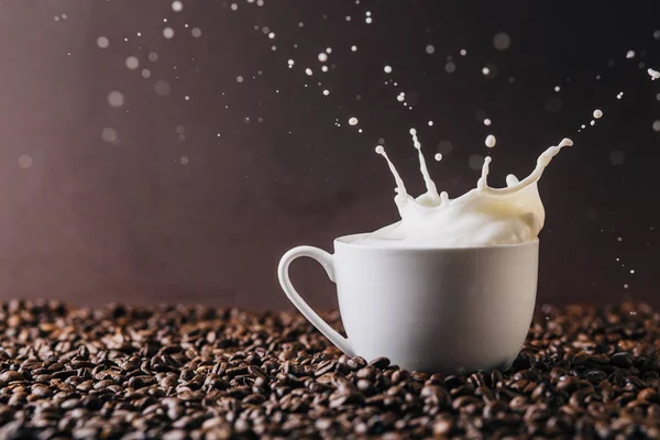 コーヒー豆で覆われたテーブルの上にミルクを振りかけるマグカップ — ストック写真