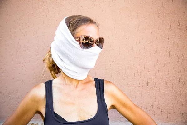 Caucasian blond woman in a white scarf put on had as a protective mask and sunglasses. Alternative to medical mask. Traveling in post pandemic world. Protection from sun, heat and dust. Summer style