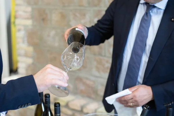 Zarif takım elbiseli iyi giyimli bir adam zevk ve zevk için zarif bir bardağa bir bardak kaliteli şarap dolduruyor.