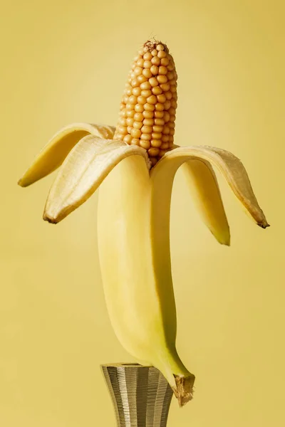 banana is displayed on an iron candlestick from which comes a corn. surealisctic image of food manipulation concept