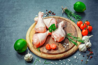 Çiğ çiğ tavuk budu, sopaları ahşap tahta, et yemek pişirmek için malzemelerle üzerinde