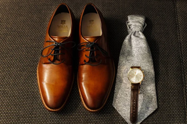 closeup of groom\'s shoes, watches and tie. getting ready. dark background