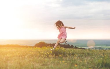 Sevimli küçük kız açık havada yaz alanına sunset bulvarında atlama uzun saçlı pembe elbiseli