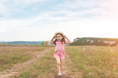 Pembe elbiseli uzun ve hasır şapka saç açık havada yaz alanına sunset bulvarında atlama ile sevimli küçük kız