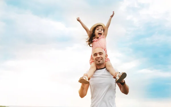 Küçük kız babasının omuzlarında oturan ve gülüyor. Yaz günü, mutlu bir aile ve yaz yaşam tarzı kavramı