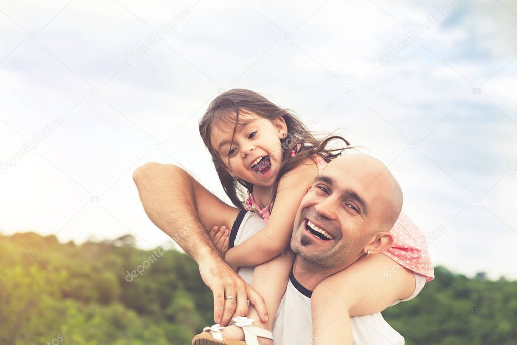 Little girl sitting on father's shoulders and laughing. Summer day, happy family and summer lifestyle concept