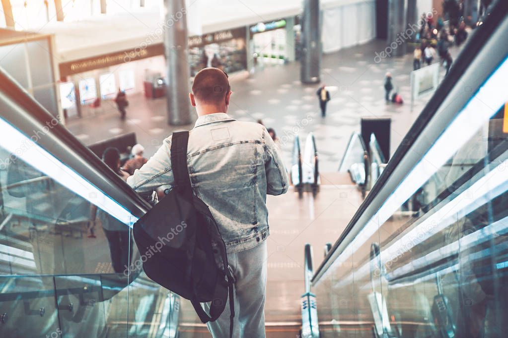 Young attractive man walking on escalator in airport building with his bag