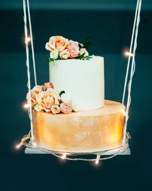 Wedding cake on decorative swing, decorated with fowers and luminous garland clipart