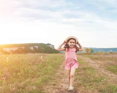 Pembe elbiseli uzun ve hasır şapka saç açık havada yaz alanına sunset bulvarında atlama ile sevimli küçük kız