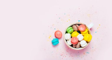 Kupası pembe bir arka plan üzerinde renkli mini macarons dolu. Metin için yer.