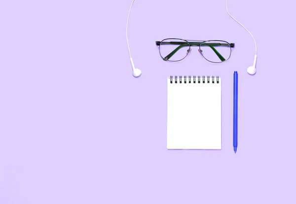 Notebook or notepad with glasses and hearphones on purple background. Creative minimalism chancery concept. Top view, flat lay.