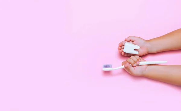 Büyük diş ve diş fırçası pembe backgroubd holding çocuğun eller. Sağlıklı bakım diş kavramı. Üstten görünüm, düz yatıyordu. Metniniz için kopya alanı.