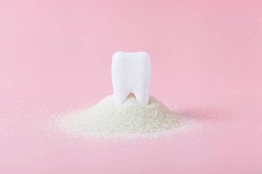 Büyük şeker yığınıiçinde plastik diş. Çürük ve şeker kavramı. Pembe arka planda diş bakımı konsepti