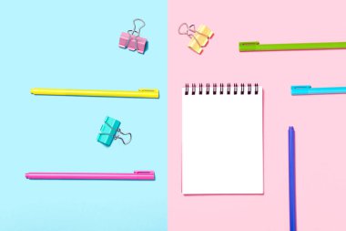 Boş Not Defteri veya not defteri mavi ve pembe arka plan üzerinde. Çeşitli kalemler. Yaratıcı minimalizm şans kavramı. Üst görünüm, düz yatıyordu.