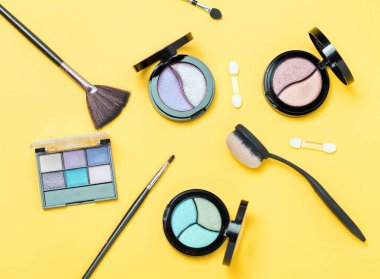 Üç Göz gölgeleri paletve çeşitli sarı arka plan üzerinde fırçalar makyaj üst görünümü. Moda kozmetik seti. Düz yatıyordu.