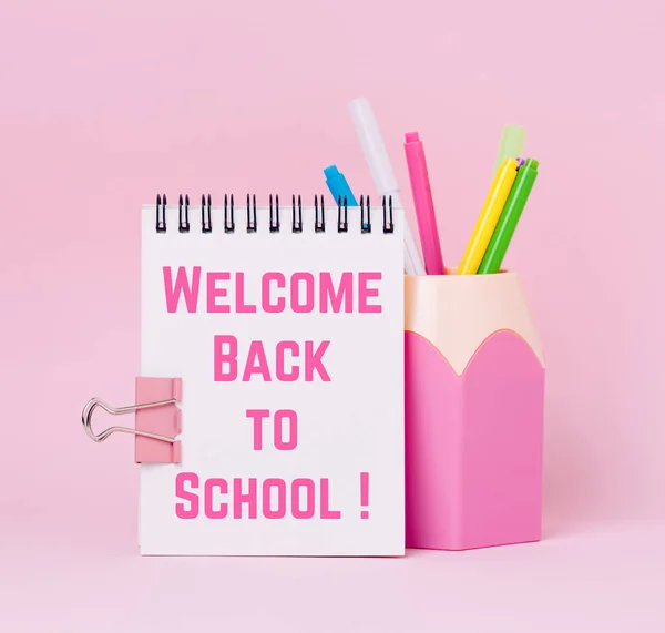 Mock up picture of notebook and pencil holder on pink background. Text \'Wellcome back to school\'.