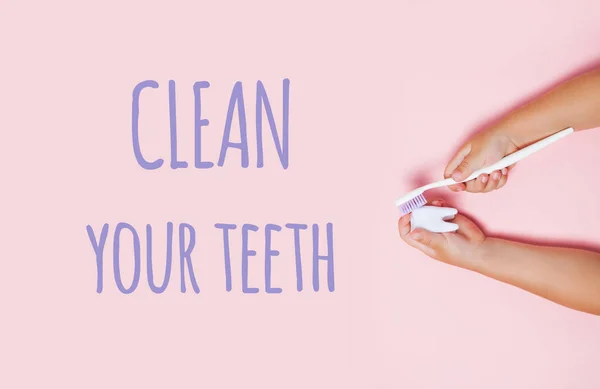 Child's hands holding big tooth and toothbrush on pink backgroubd. Healty care teeth concept. Top view, flat lay. Clean your teeth text.