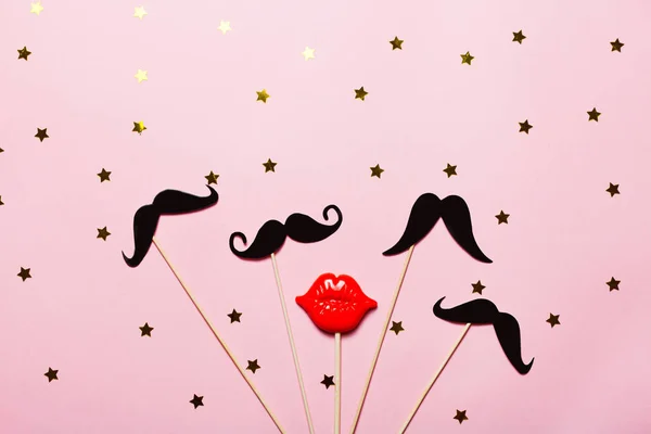 Birçok kağıt bıyık ve sopa ile yıldızlar ve konfeti pembe arka plan üzerinde kırmızı plastik dudaklar. Parlak ve festival resim, maskeli balo ve Movember kavramı. Üstten görünüm, düz yatıyordu.