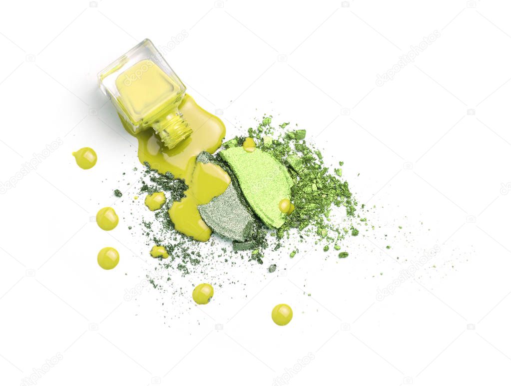 Spilled nail polishes bottles on lime and yellow eye shadows cosmetic. Isolated on white. Creative cosmetic concept.