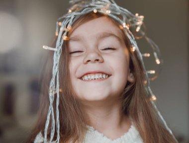 Sevimli küçük gülümseyen kız başında Noel ışık saçan garland ile.