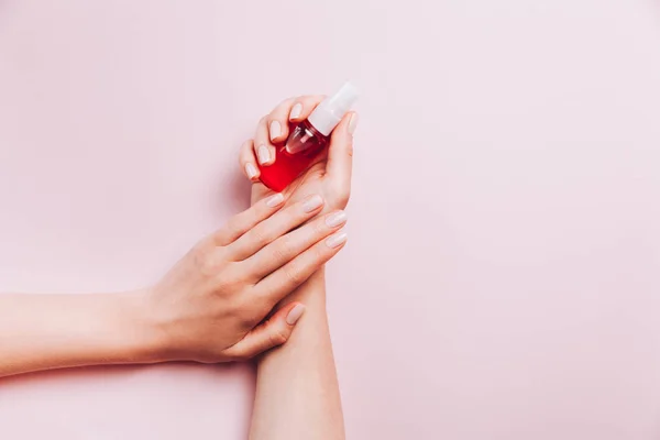 Manicura femenina de moda. Las manos de la mujer sosteniendo tratamiento de uñas sobre fondo rosa . — Foto de Stock