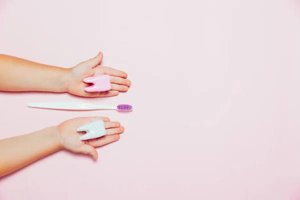 Manos de niño sosteniendo gran diente y cepillo de dientes en el fondo rosa. Concepto de dientes de cuidado de salud. Vista superior, cama plana. Copia espacio para tu texto . — Foto de Stock