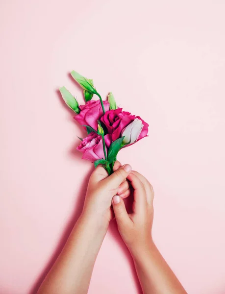 Little children hands holding beautiful flowers on pink background. — Stock Photo, Image
