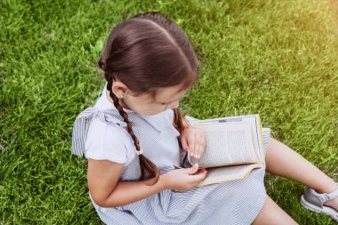 Kitap okurken çimin üzerinde örgü ören tatlı bir kız öğrenci. Eğitim, öğrenme ve okul konseptine geri dönüş. Evde eğitim.