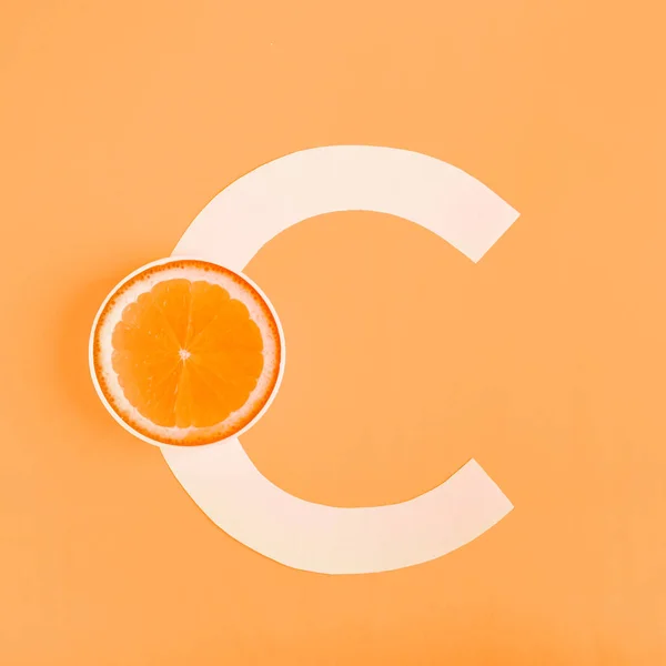 Laranja e letra C num fundo amarelo. O conceito de Vitamina C. Proteção do outono contra resfriados, antioxidante — Fotografia de Stock