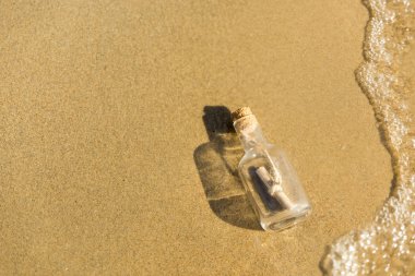 Bir şişe bir mesaj ile bir kumsala bir dalga tarafından atılır. Sandy arka plan. Şişe sörf satırında yüzer. Alan üst görünüm Kopyala
