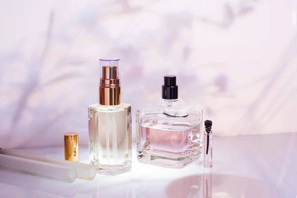 不同的香水瓶和采样器在粉红色的花卉背景。选择性对焦。香水收藏, 化妆品 — 图库照片