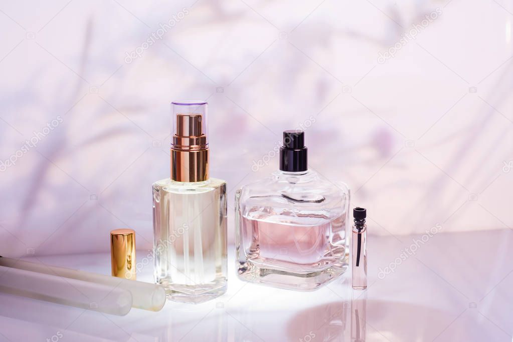 Different perfume bottles and sampler on a pink floral background. Selective focus. Perfumery collection, cosmetics